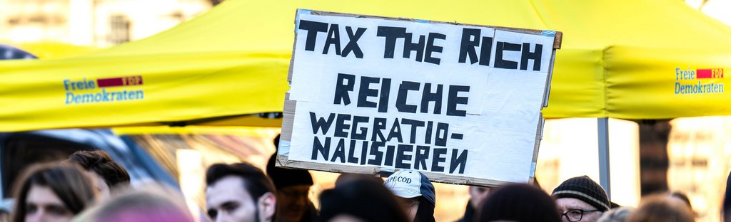 «Tax the Rich (Besteuerung der Reichen) - Reiche wegrationalisieren» steht auf einem Protestplakat bei einer Wahlkampfveranstaltung der FDP am 13.1.2025 auf dem Bremer Marktplatz. 